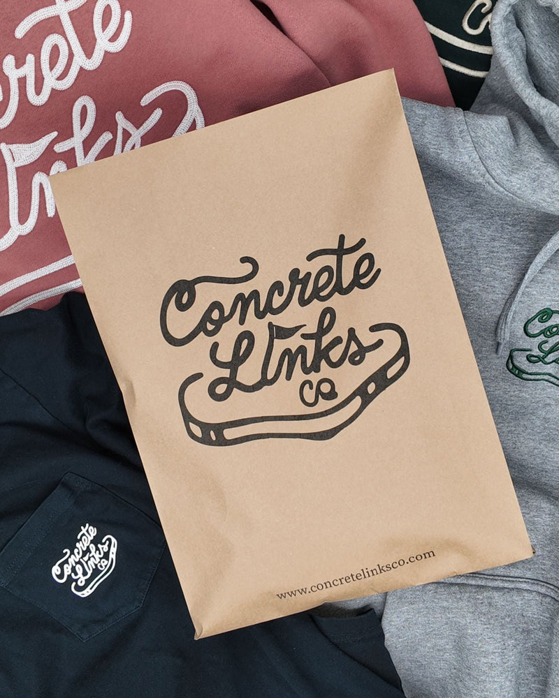Kraft paper bag with 'Concrete Links' branding on a background of clothing.