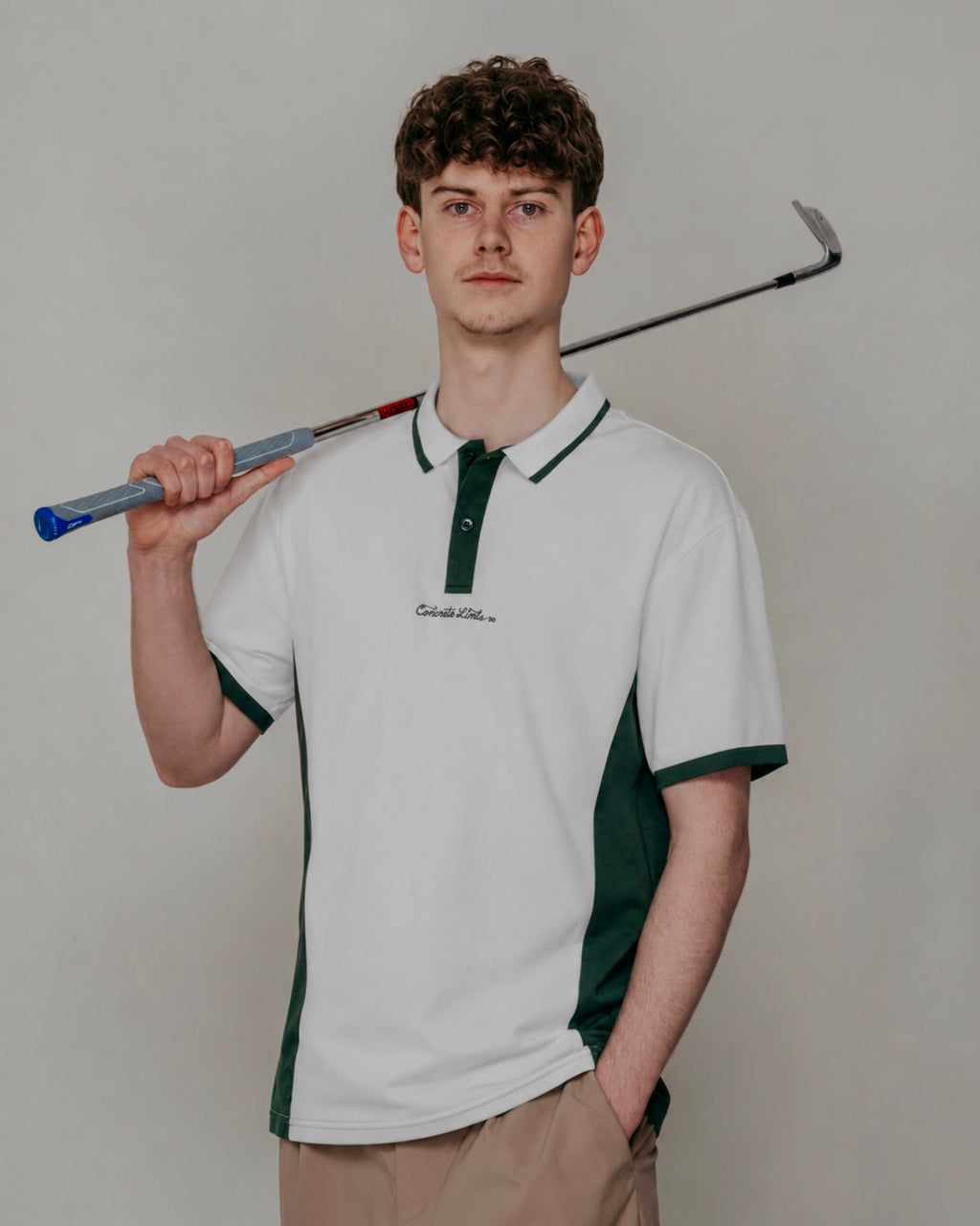 Person wearing a white and green polo shirt holding a golf club against a plain background