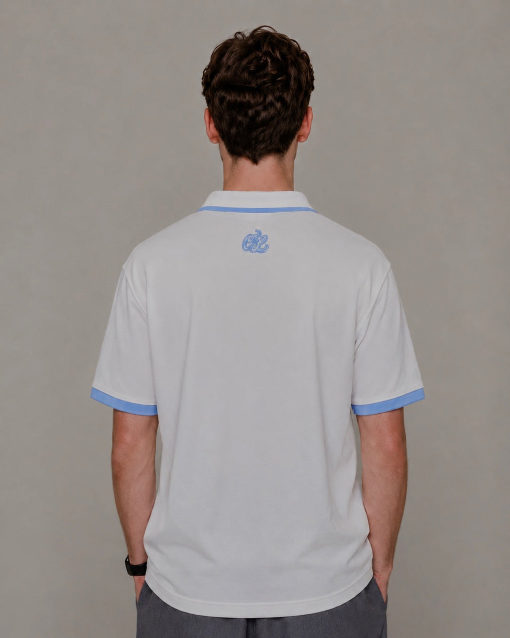 Person wearing a light gray polo shirt with blue trim on a plain background