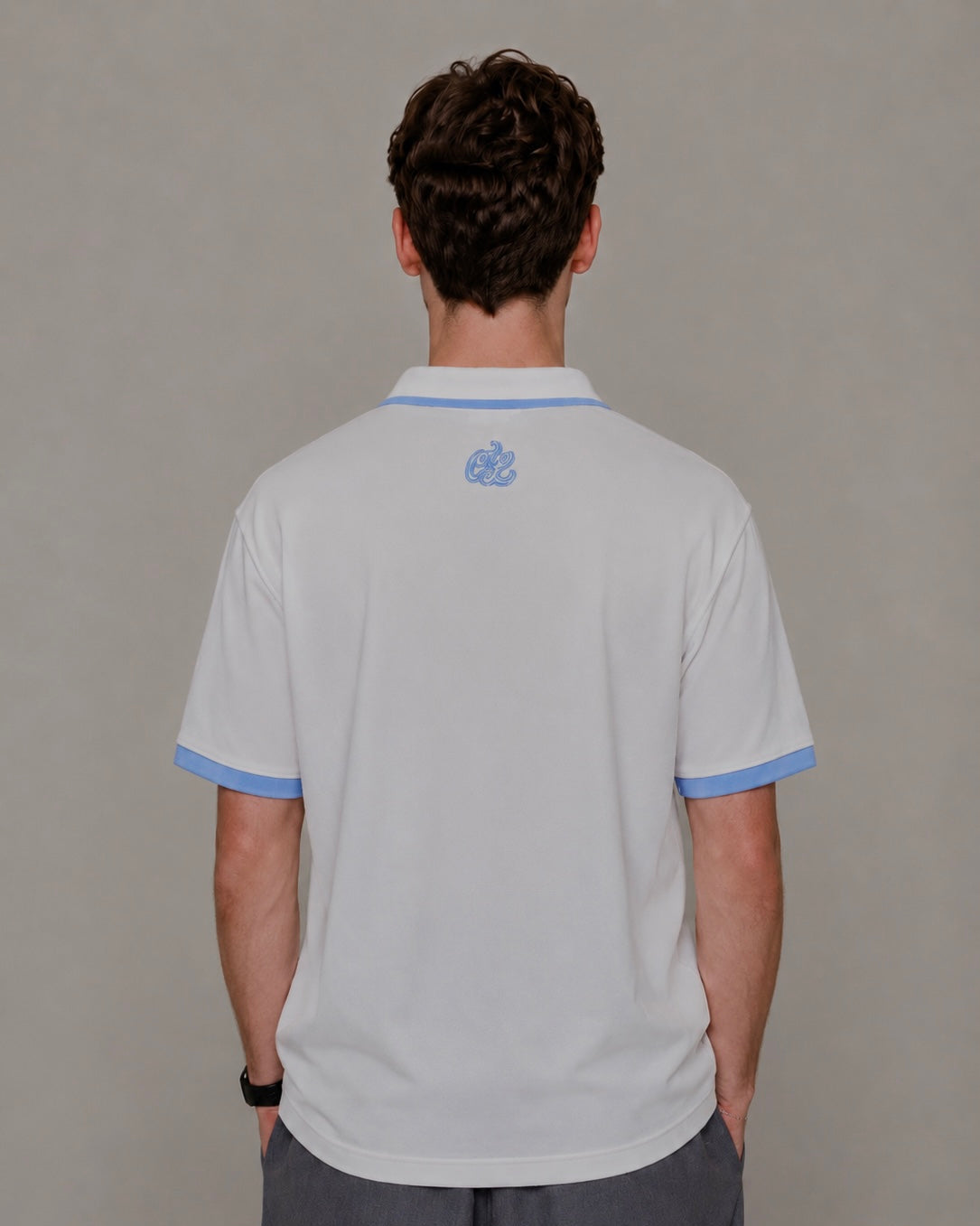 Person wearing a light gray polo shirt with blue trim on a plain background