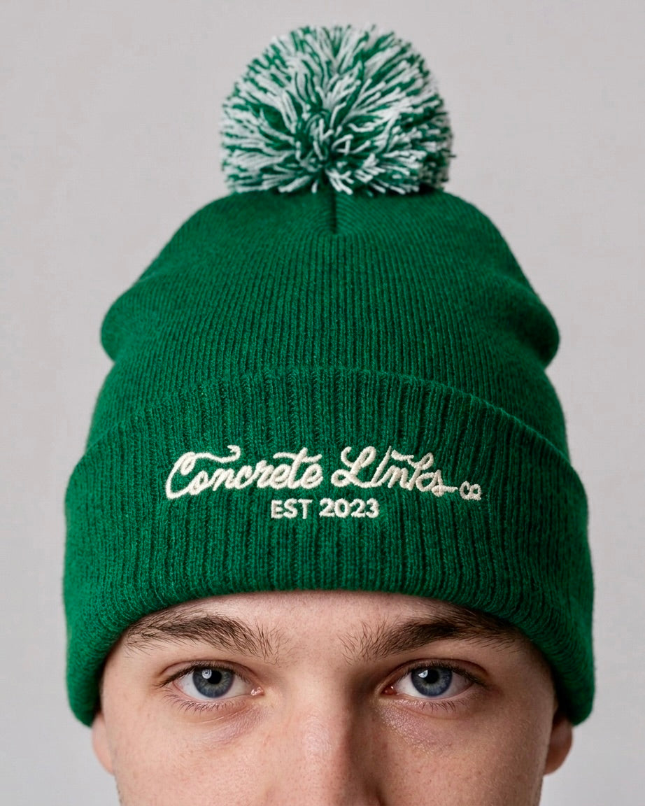Green beanie with pom-pom and 'Concrete Limits' logo on a gray background