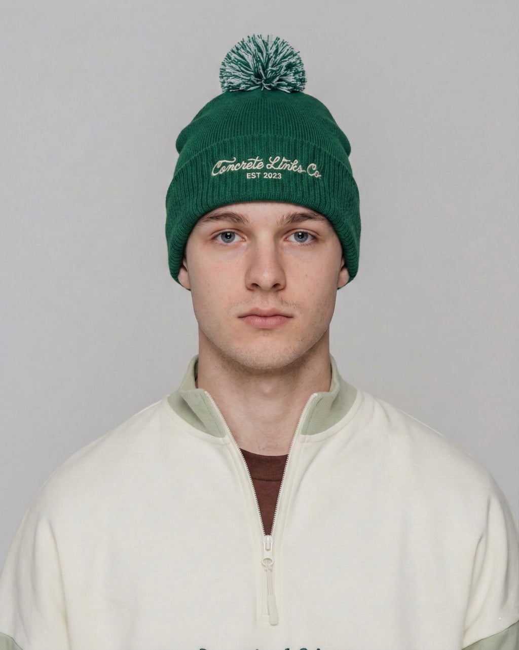 Person wearing a green beanie with branding on a plain background