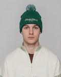 Person wearing a green beanie with branding on a plain background