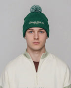 Person wearing a green beanie with branding on a plain background