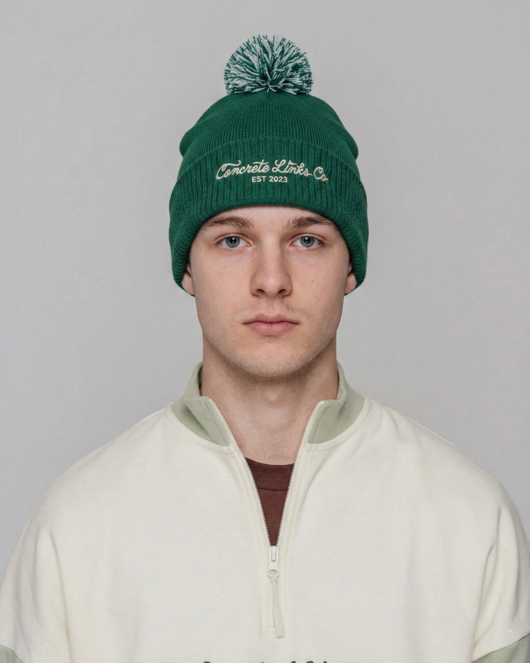 Person wearing a green beanie with branding on a plain background