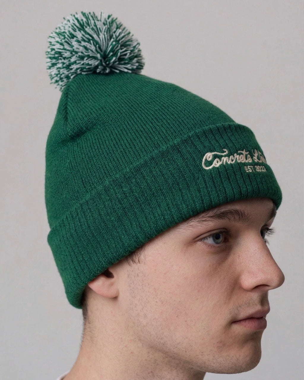 Green beanie with pom-pom worn by a person on a plain background