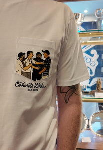 White t-shirt with a graphic design on the chest pocket, featuring text 'Concrete Links EST 2023'. Shows the fights by Rory Mcilroy in the car park in 2013 at Marco Simone at the Ryder Cup
