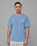 Man wearing a light blue t-shirt with a logo on a gray background