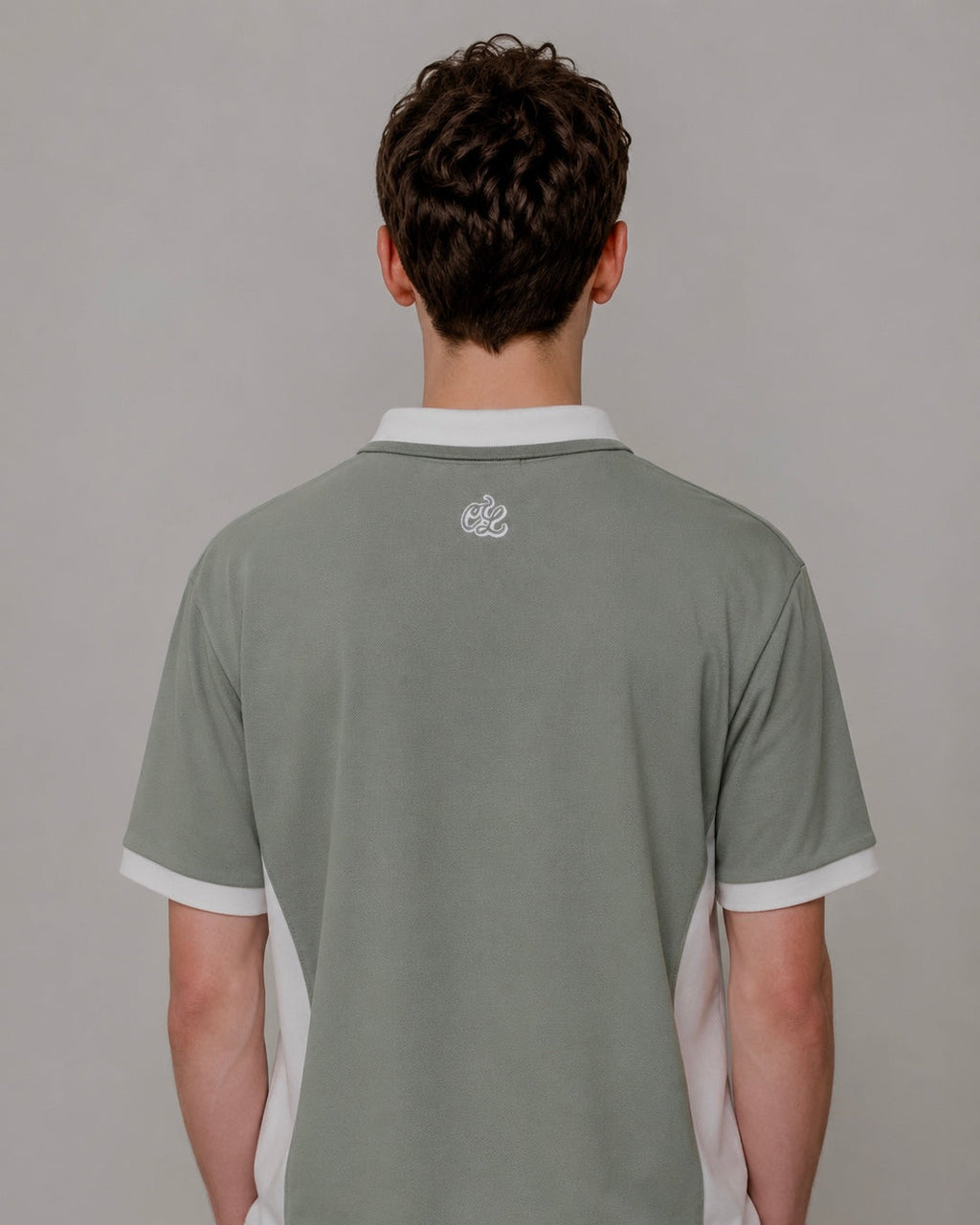 Person wearing a gray polo shirt with a small logo on the chest against a plain background