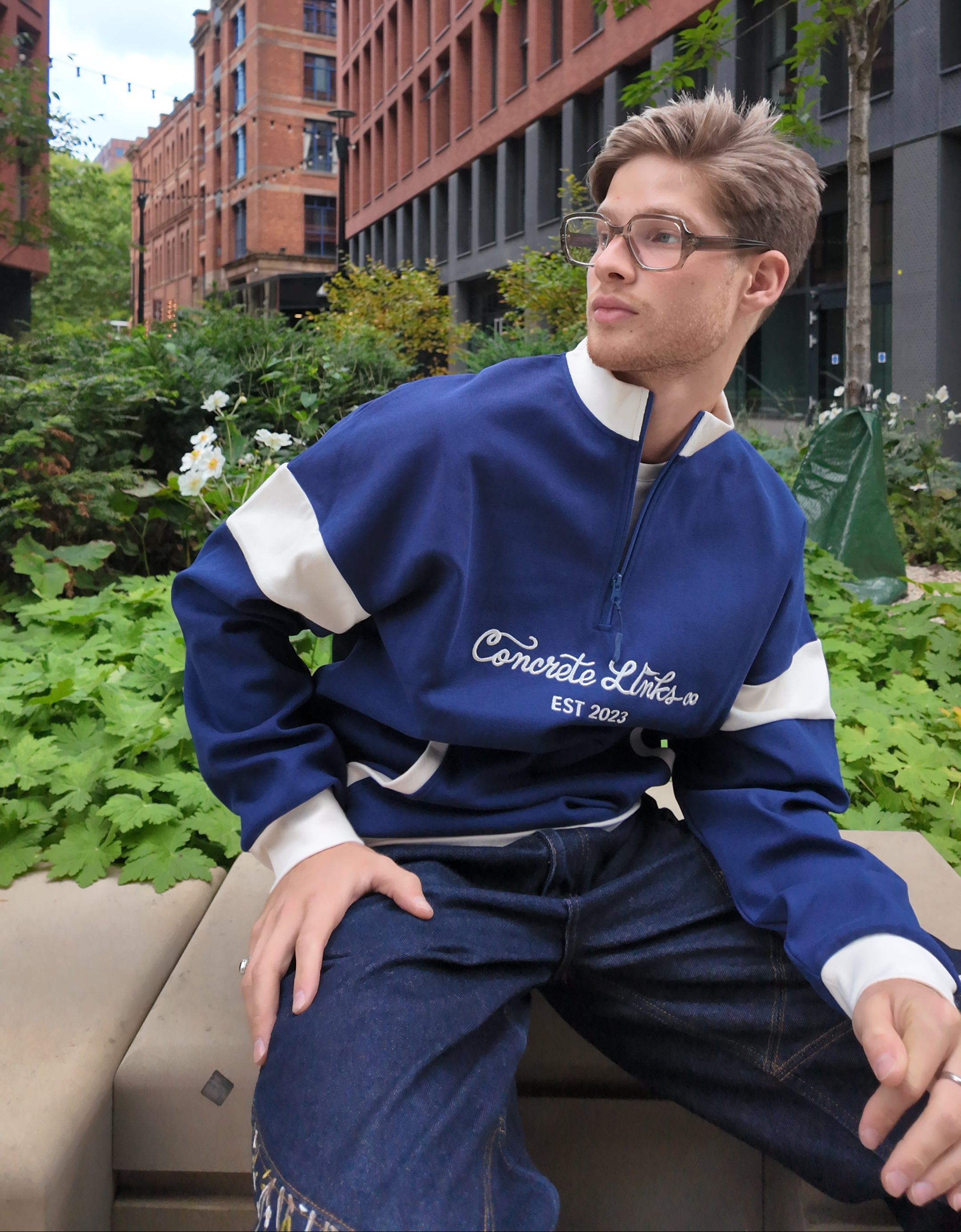 Person wearing a blue jacket with white accents sitting on a bench outdoors.