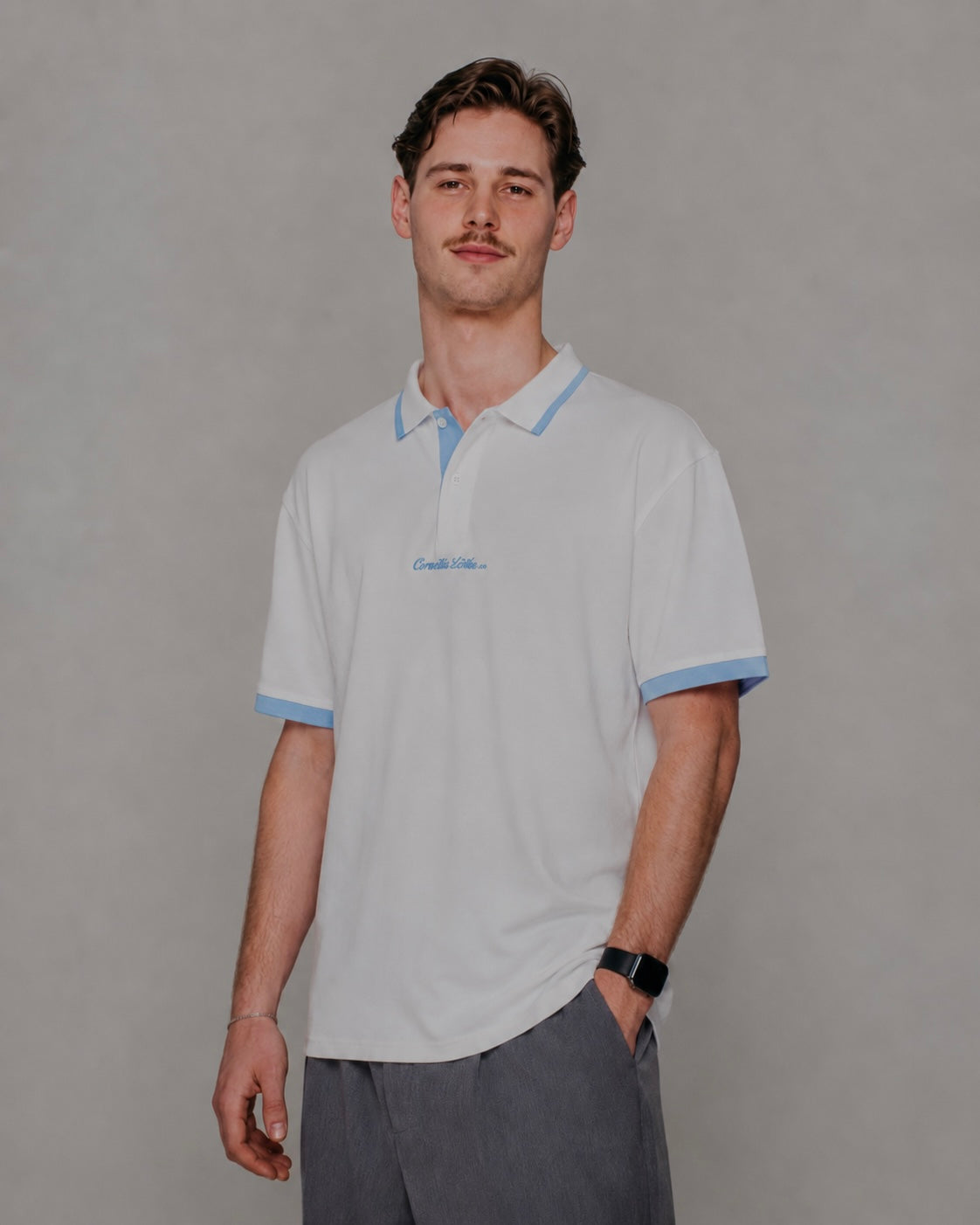 Man wearing a light gray polo shirt with blue trim on a plain background