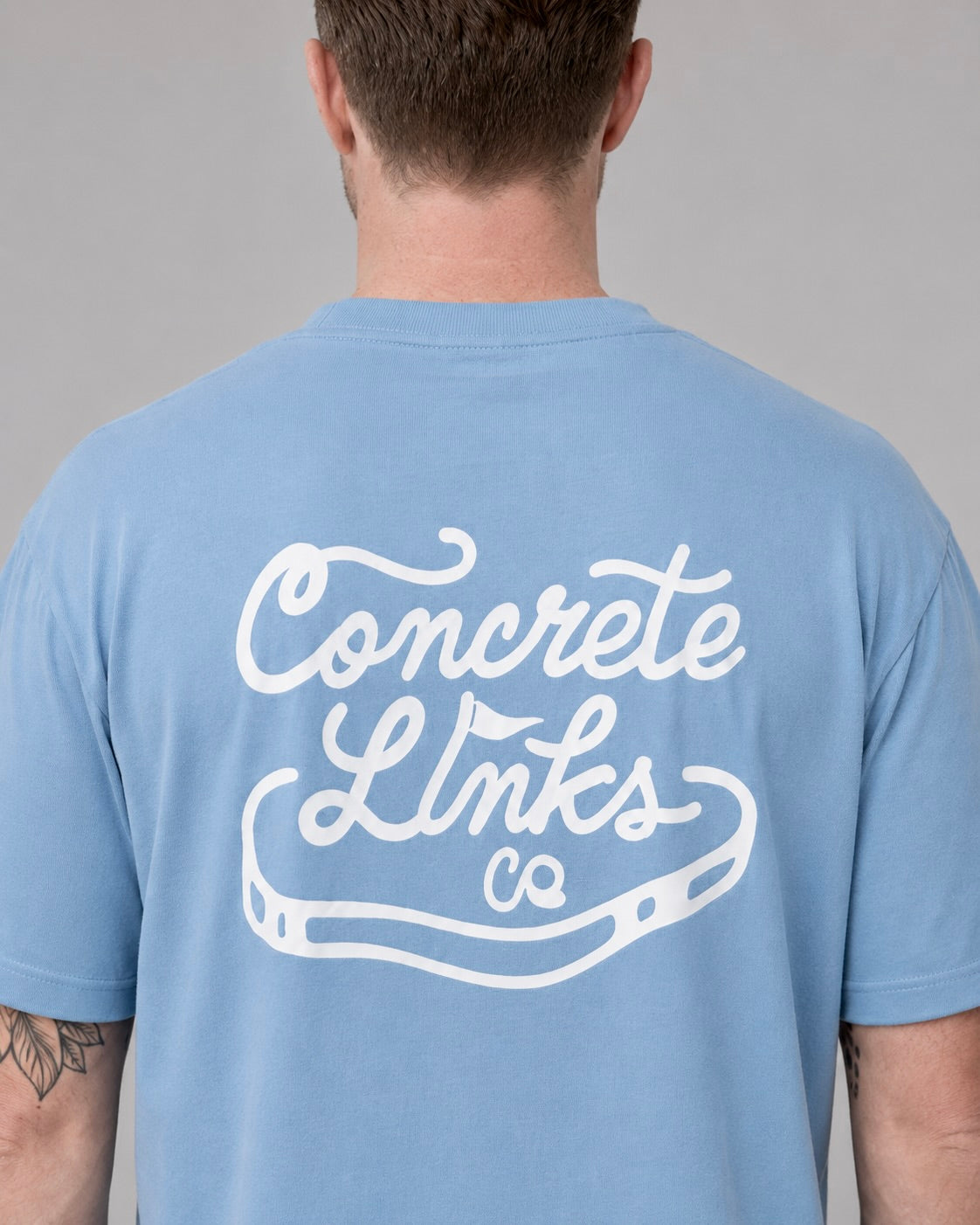 Person wearing a light blue t-shirt with 'Concrete Links Co' printed on the back against a gray background